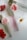 Three perfume bottles with elegant gold caps are arranged alongside vibrant red and white flowers on a sleek, white surface.
