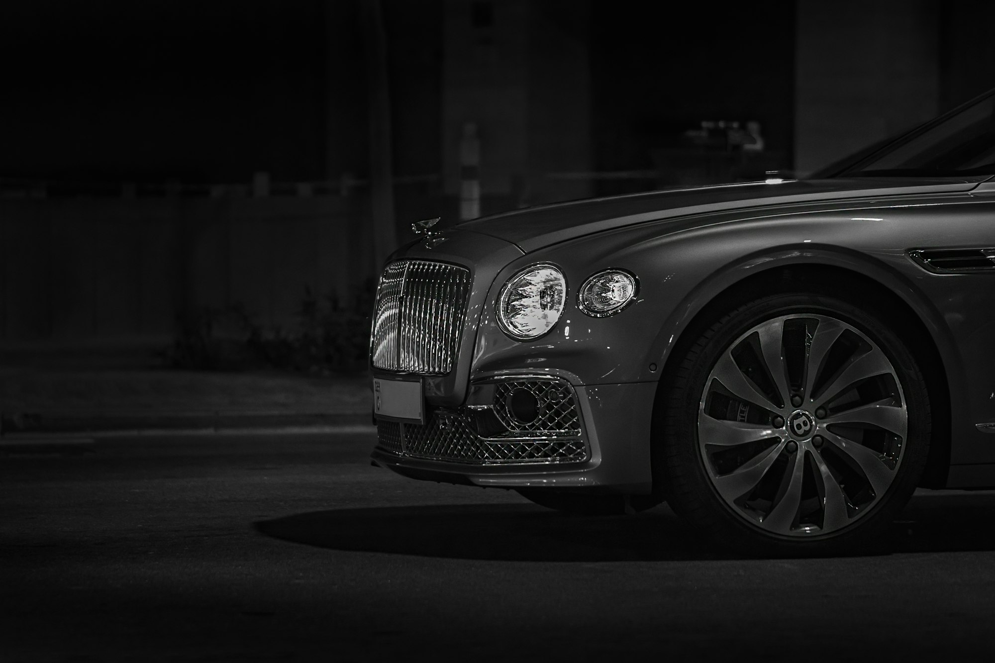 A grey Bentley out at night with only the front part shown