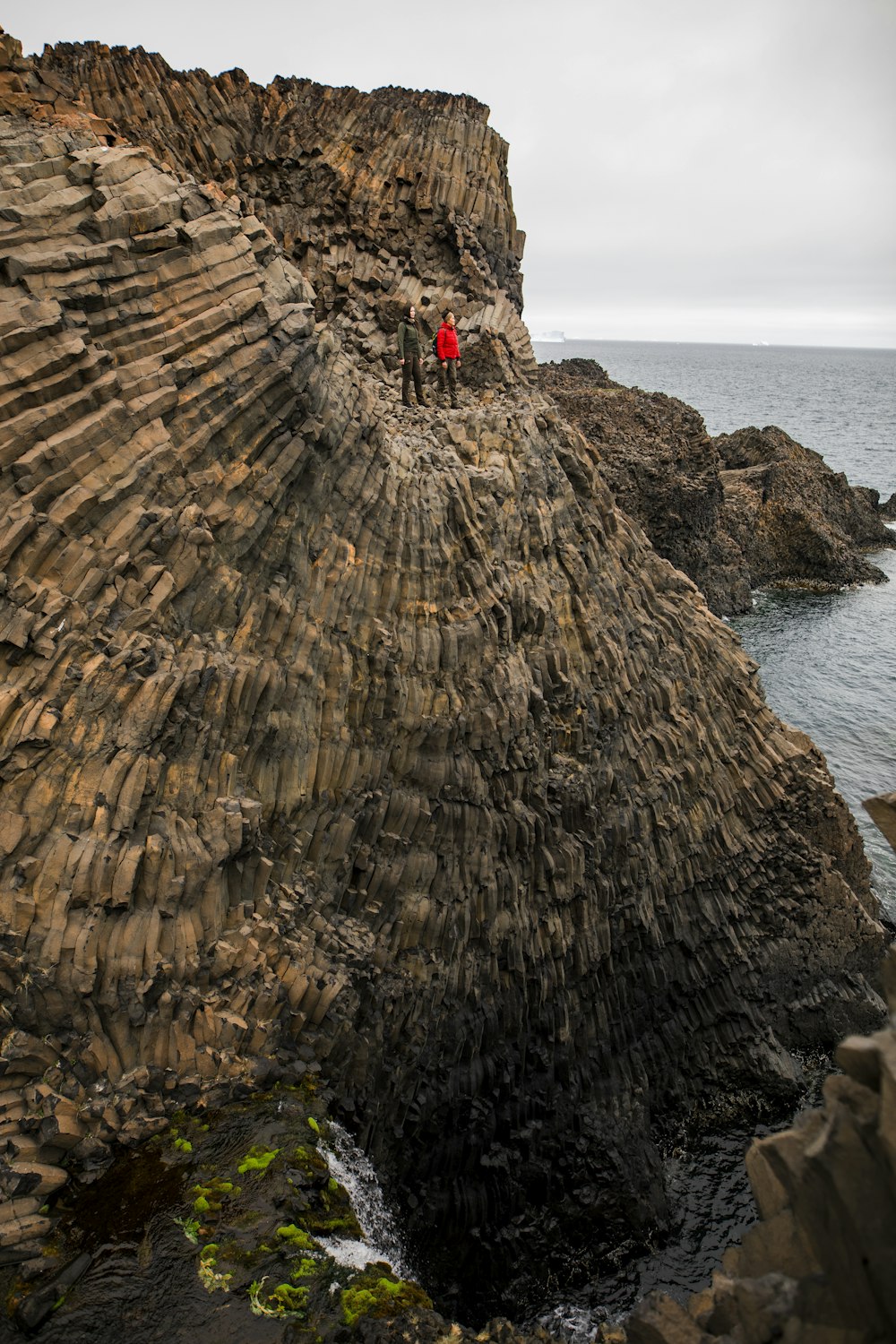 person in red shirt standing on brown rock formation near body of water during daytime