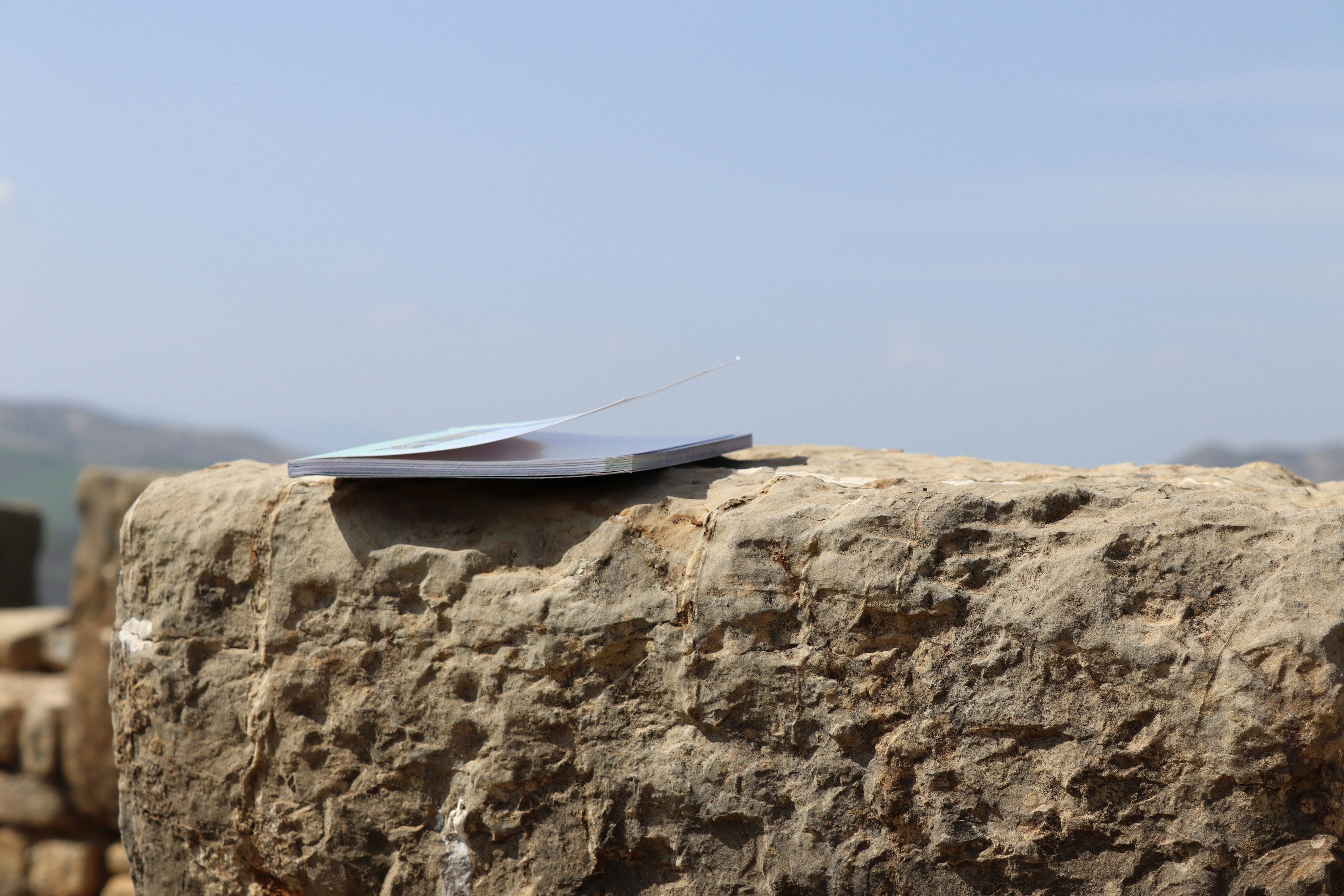 Open book with pages fanned out on rocky mountain terrain under blue sky
