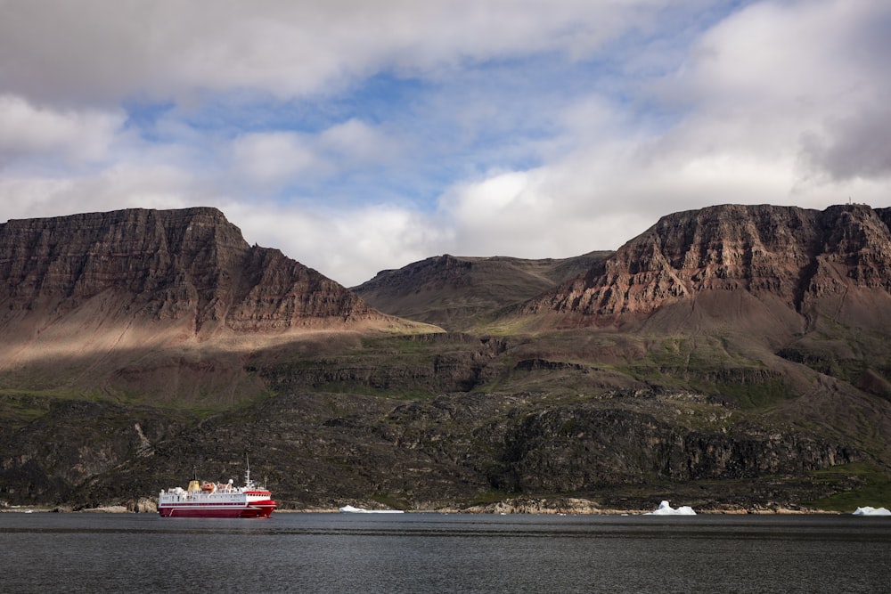 red and white boat on body of water near brown mountain during daytime