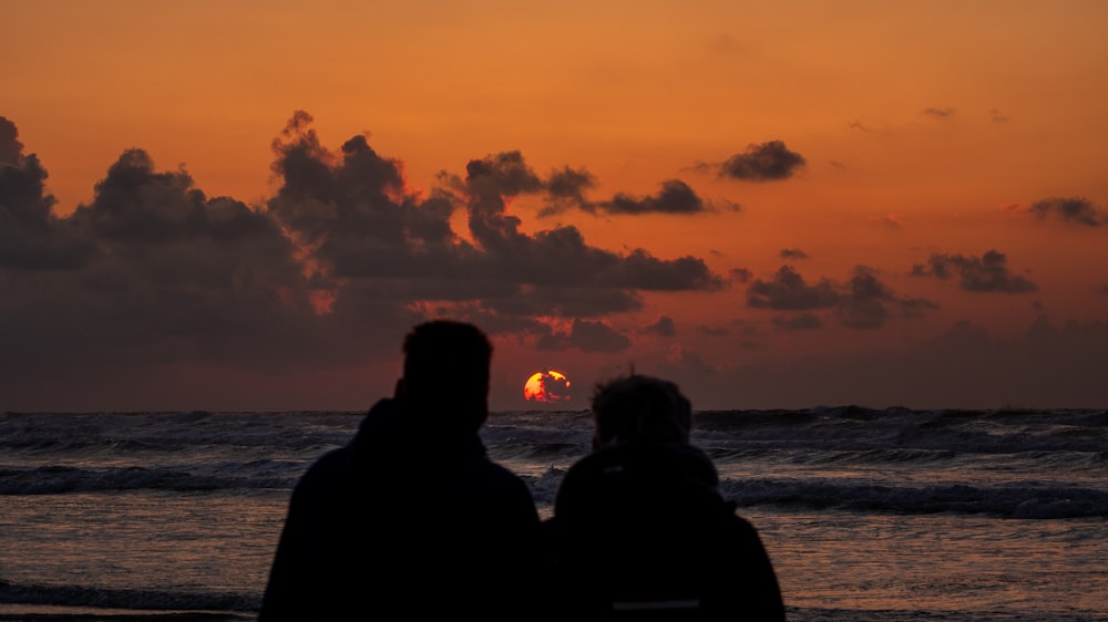 silhouette of 2 person standing near body of water during sunset