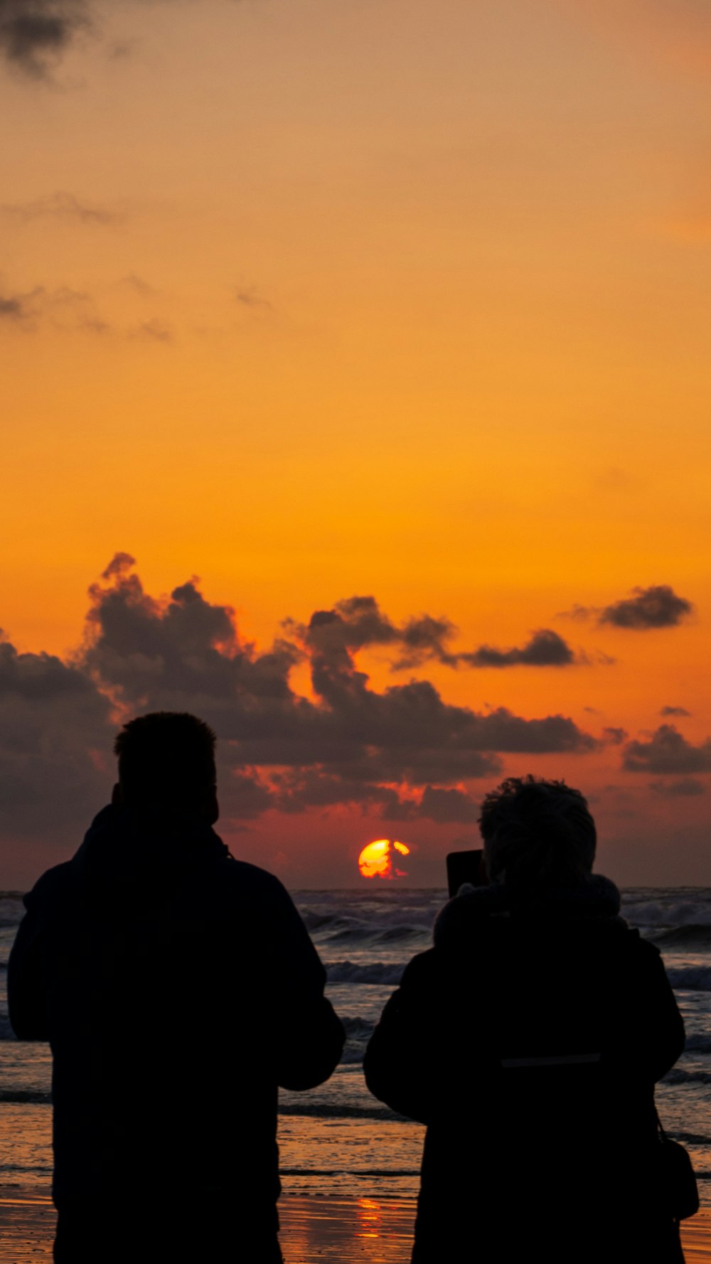 silhouette of couple standing near body of water during sunset