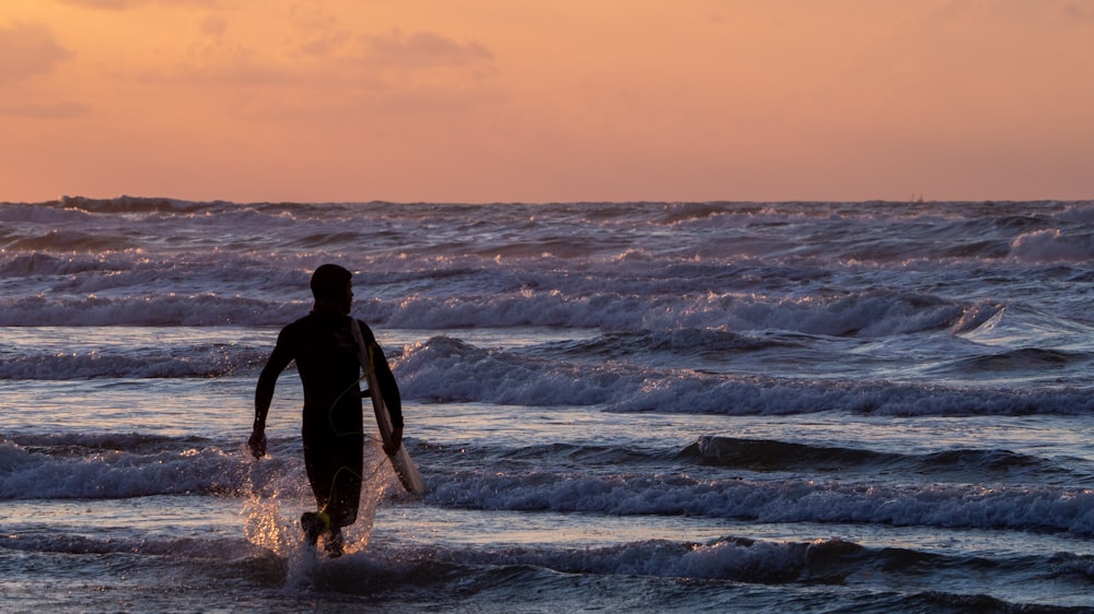 man in black wet suit standing on sea shore during sunset