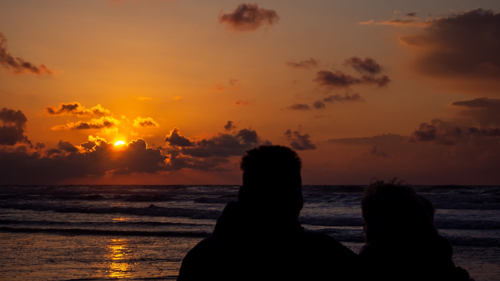 silhouette of man and woman standing near sea during sunset