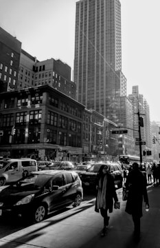 High-contrast black and white cityscape showing bustling street life under dramatic shadows.
