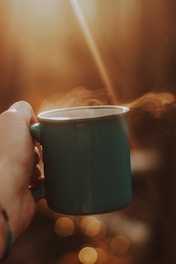 Close-up of hands holding a steaming mug by a softly lit window.