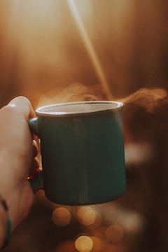 Close-up of hands holding a steaming mug by a softly lit window.