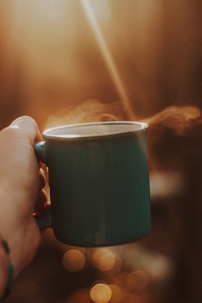 A close-up of a hand holding a beautifully designed cuddle cup mug filled with steaming tea, soft natural light highlighting the cozy details.