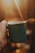 A close-up of a hand holding a bright, hand-thrown ceramic mug filled with steaming tea, sunlight casting soft shadows.