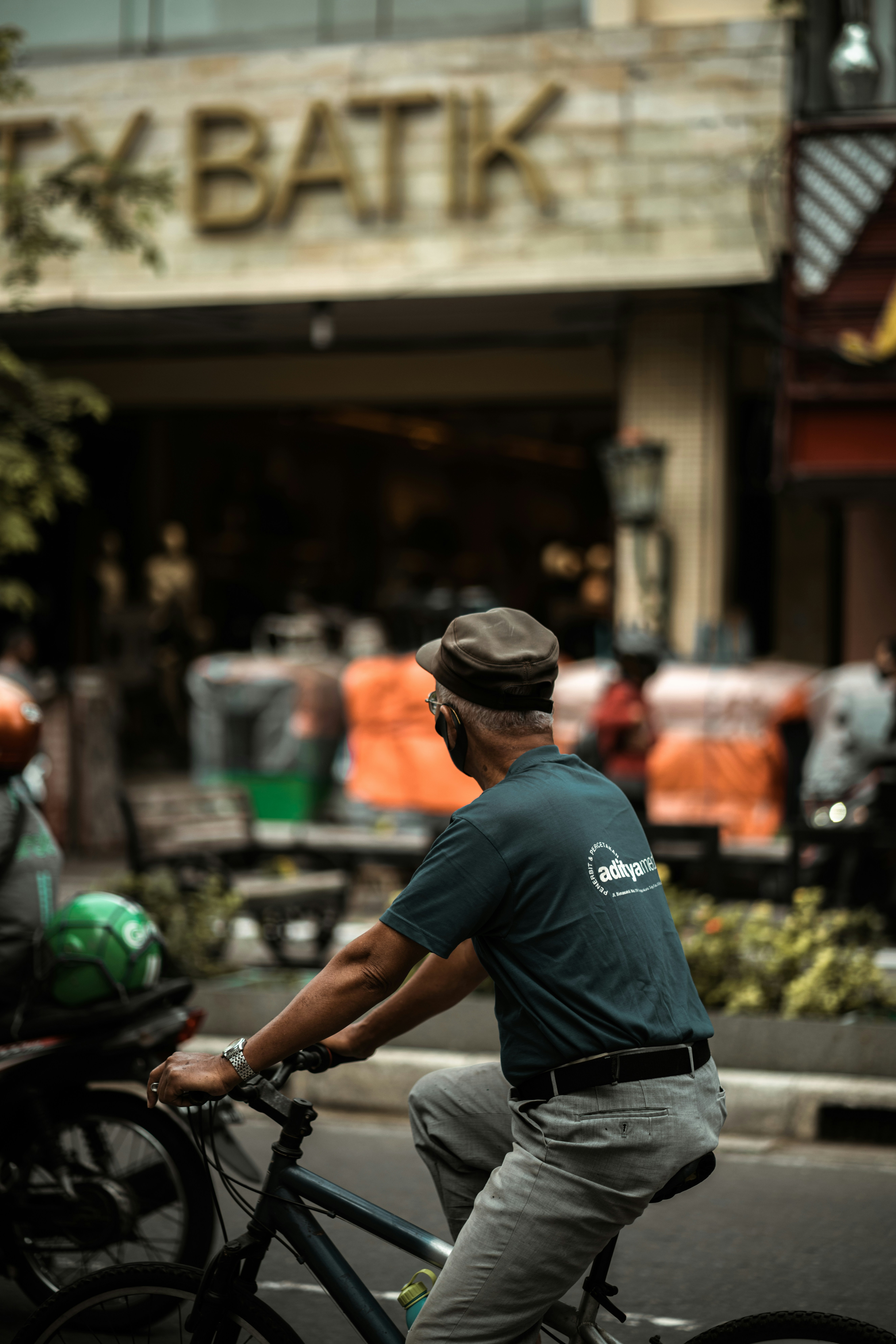 Pria berkaos biru dan topi hitam mengendarai sepeda motor di siang hari