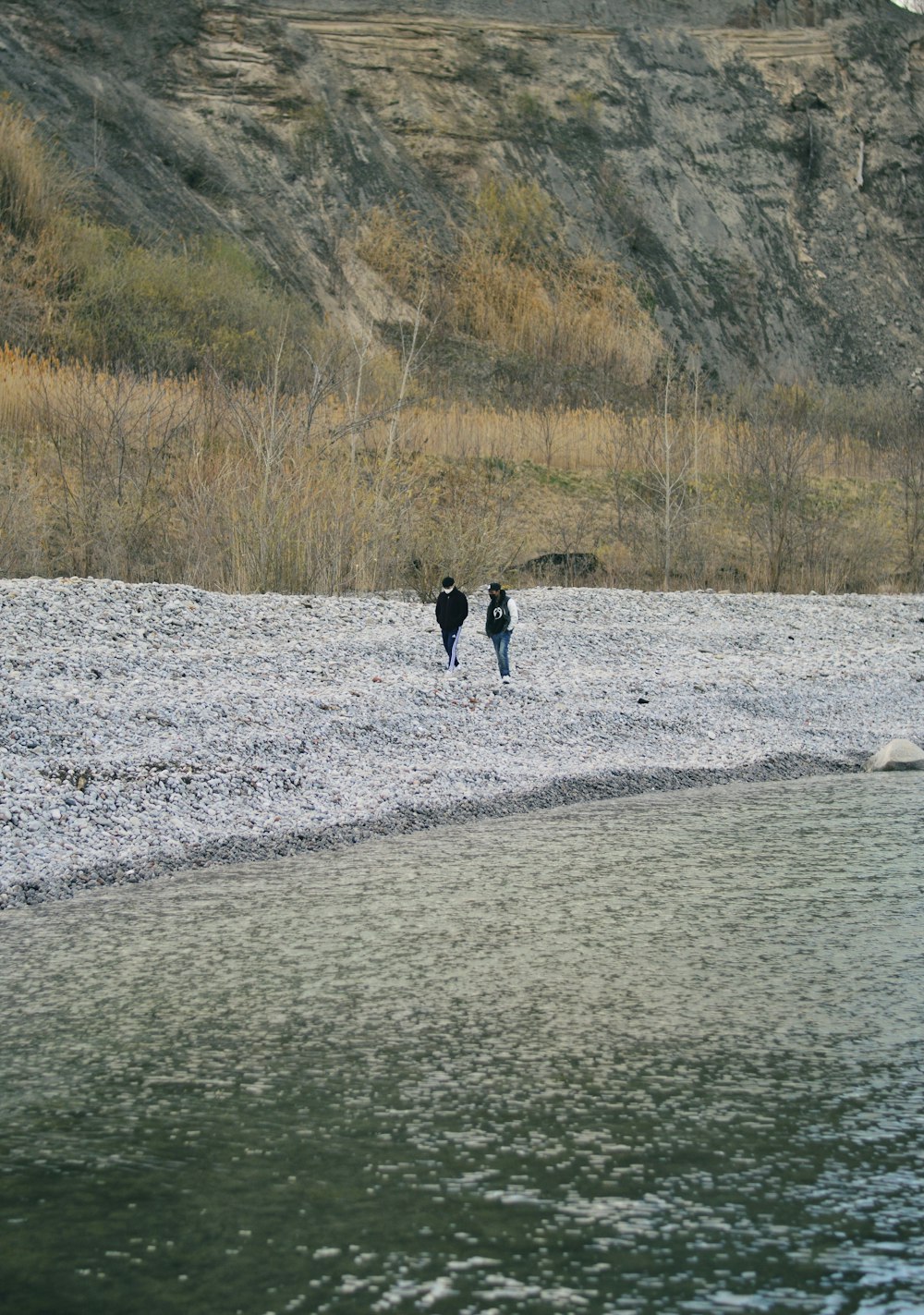 person in black jacket walking on gray sand near body of water during daytime