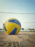 A close-up of a player holding a royal blue and white official match volleyball on an outdoor court.