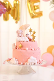 A beautifully decorated cake with pastel colors and baby-themed toppers for a full moon celebration.