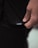 A close-up image of a person's hand holding the hem of a black garment with a small white label displaying the letters 'LSKD'. The lighting is soft, creating subtle shadows and highlights on the fabric and skin.