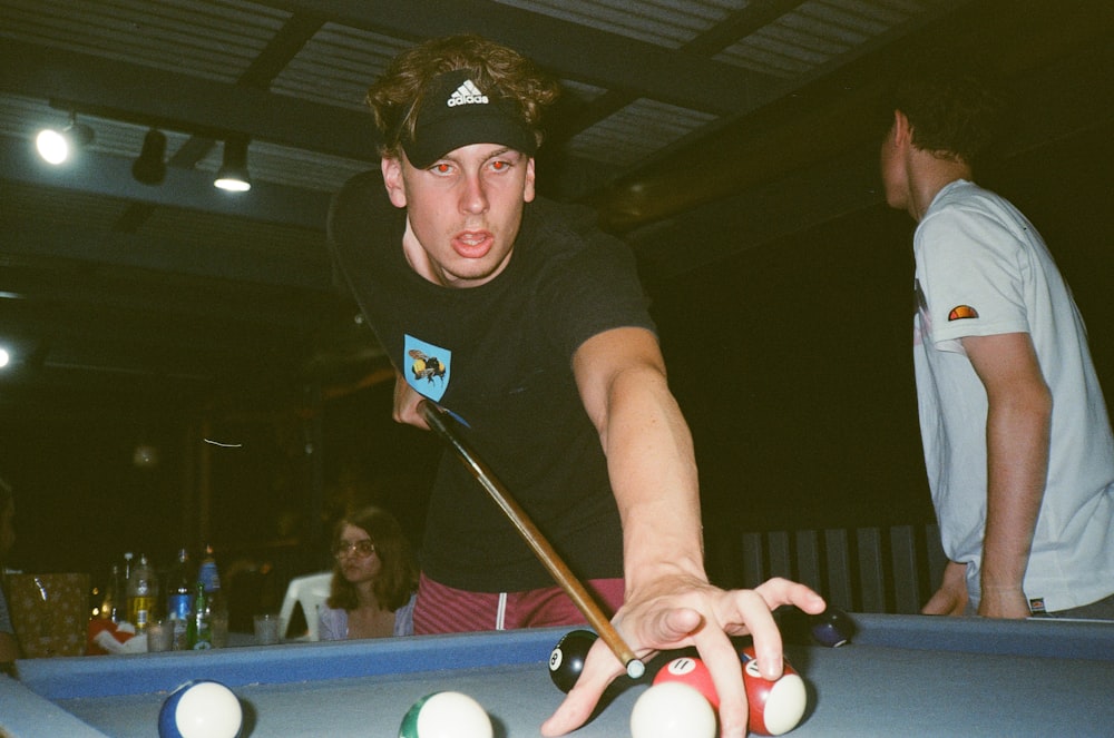 man in black crew neck t-shirt and black fitted cap playing billiard