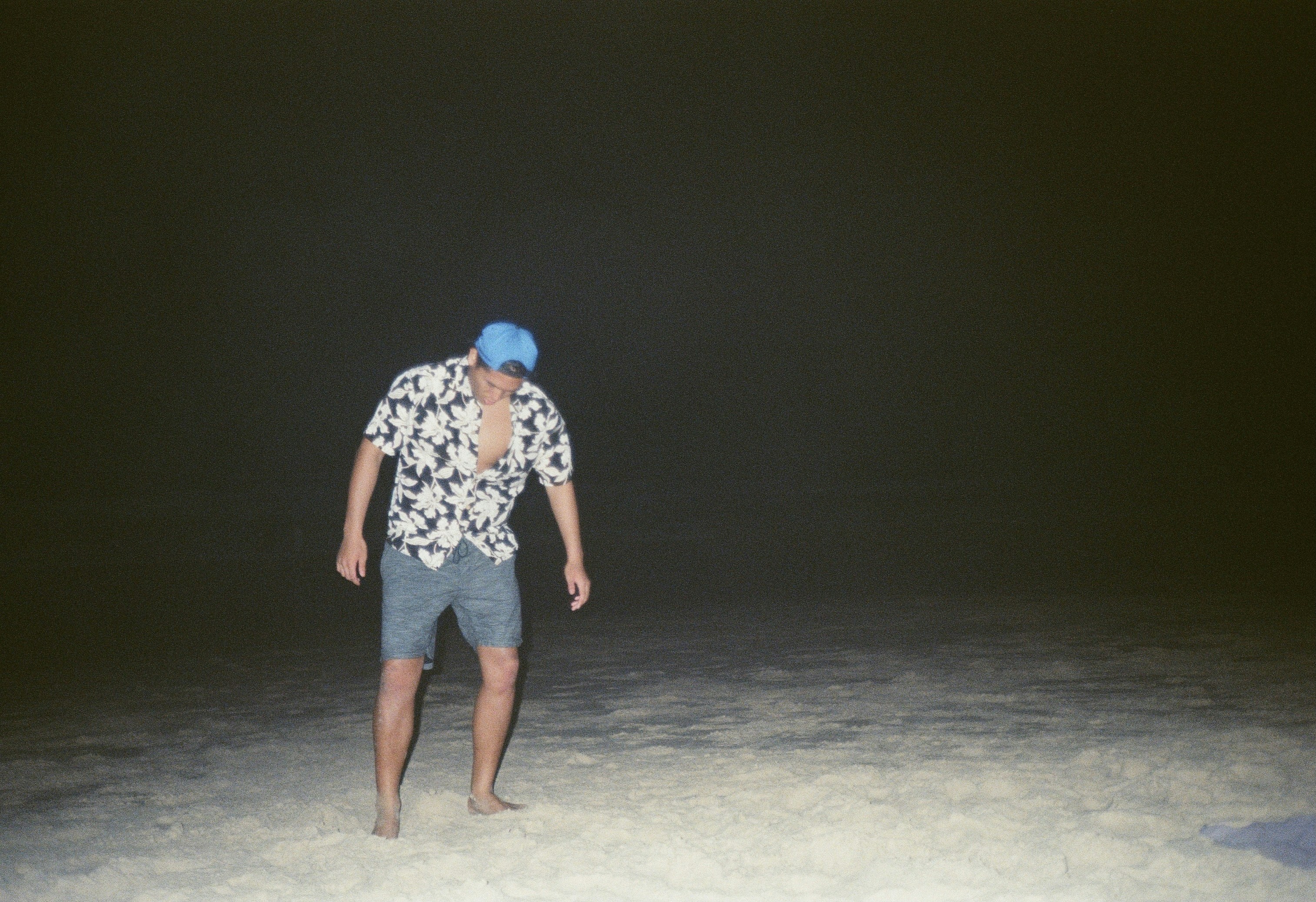 mujer con camisa floral blanca y negra y pantalones cortos de mezclilla gris de pie sobre arena gris durante