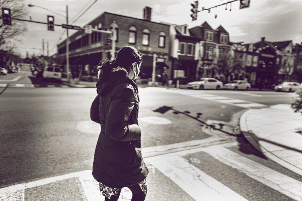 Photo en niveaux de gris d’une femme en veste noire debout sur le trottoir