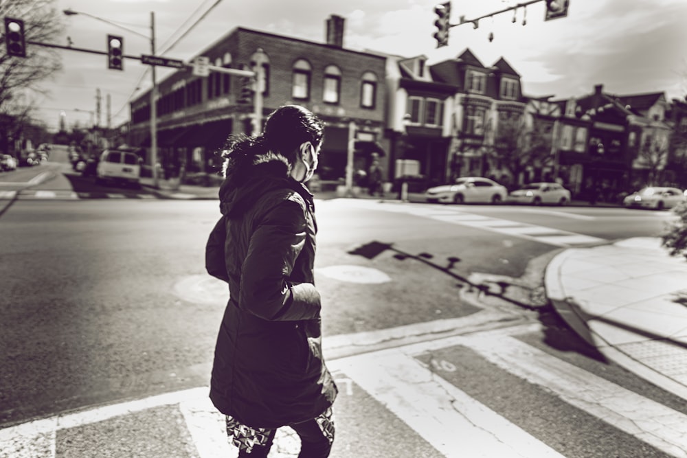 grayscale photo of woman in black jacket standing on sidewalk