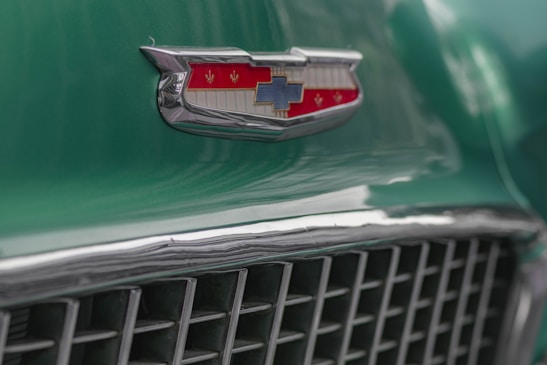 Close-up shot of a polished chrome car grille with a classic American flag reflected in it.
