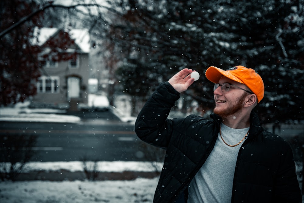 homme en veste noire et casquette orange tenant une casquette orange