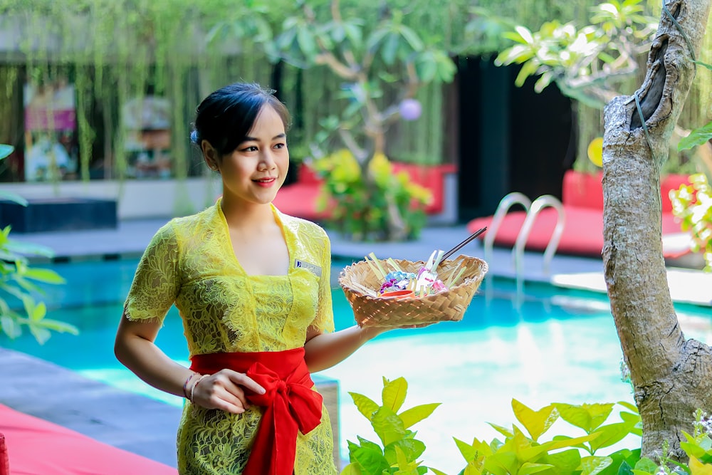 woman in yellow and red dress holding basket full of fruits