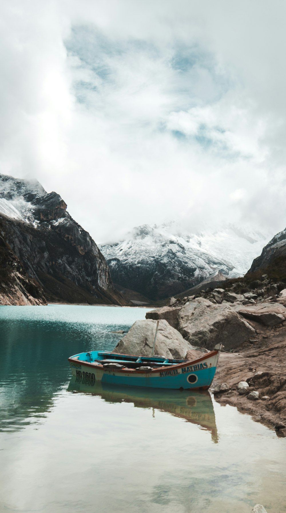 blue and white boat on brown rocky shore near mountain during daytime