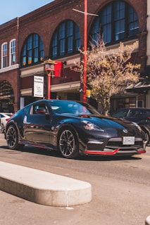 A sleek black sports car with custom matte finish and red accents parked on a city street at dusk