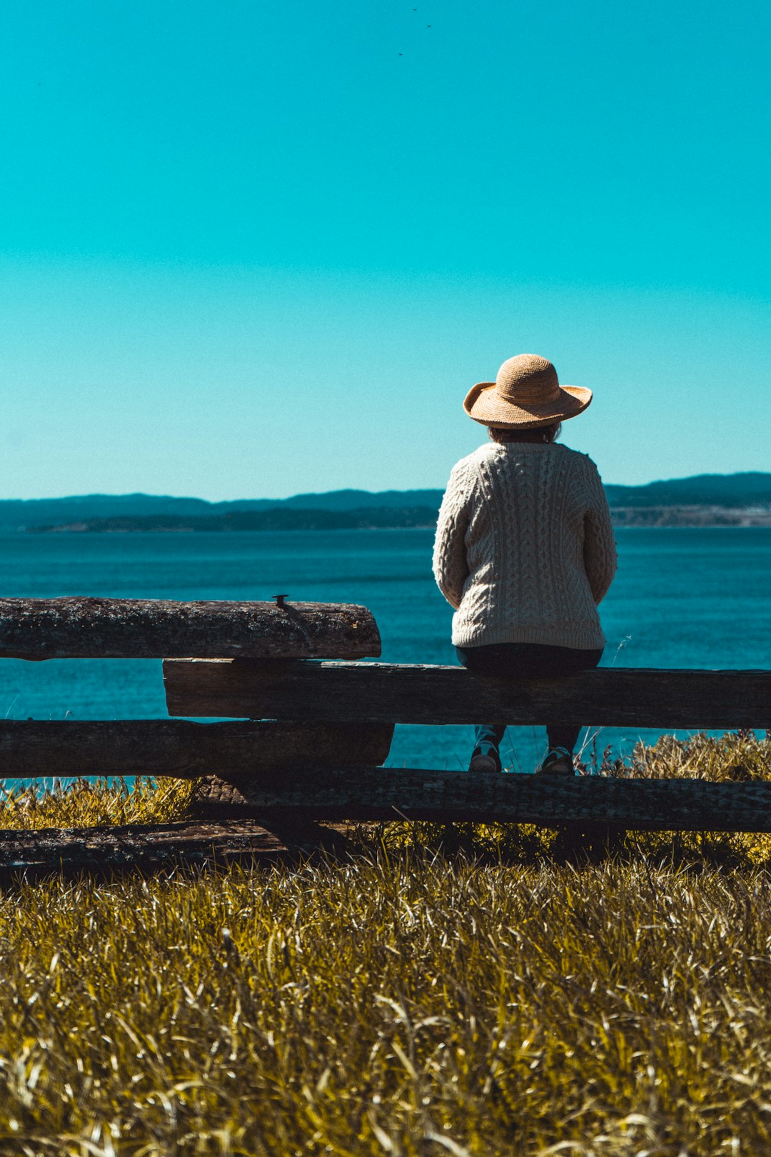 woman in white long sleeve shirt sitting on bench looking at the sea during daytime