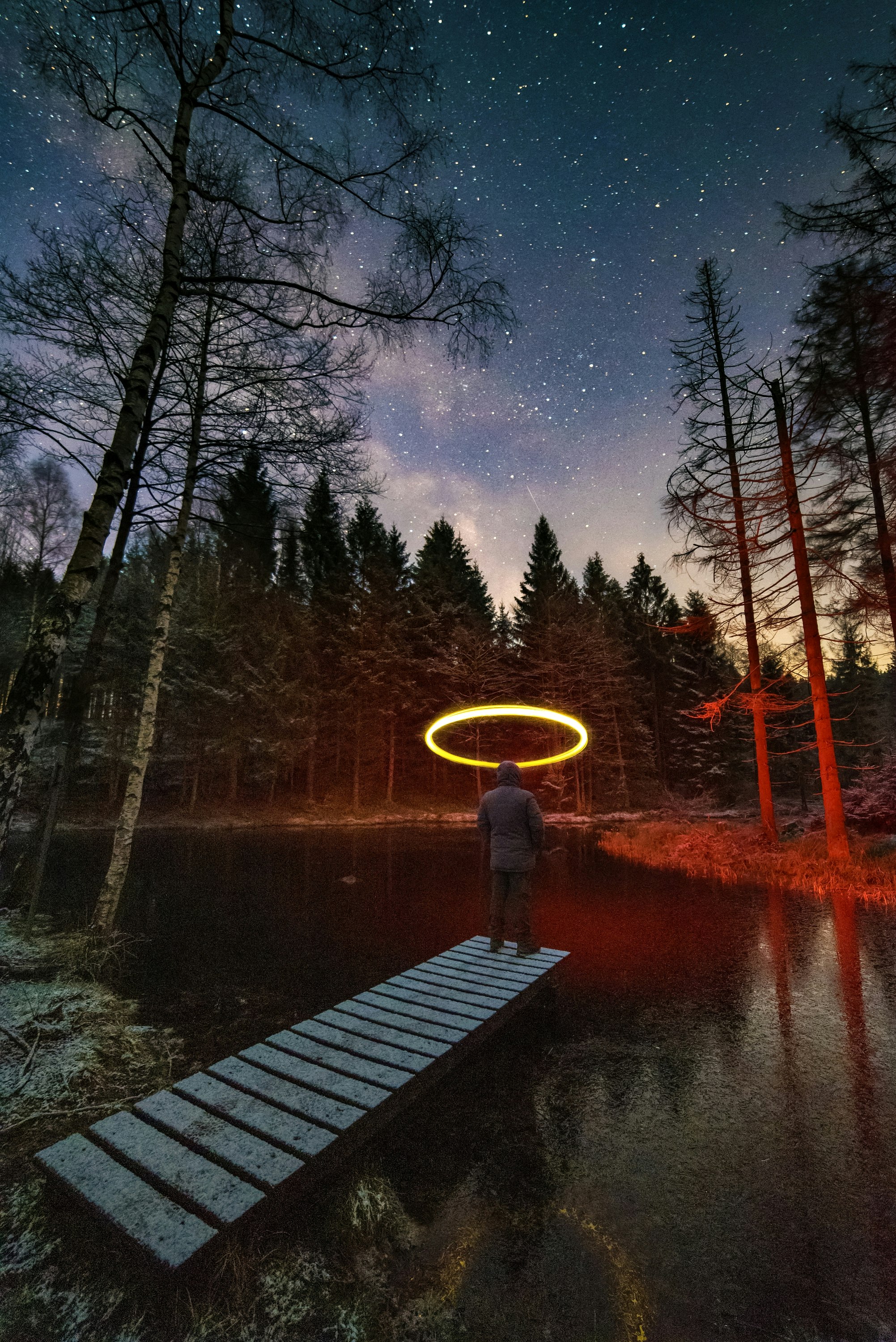 person standing on wooden dock near body of water during night time