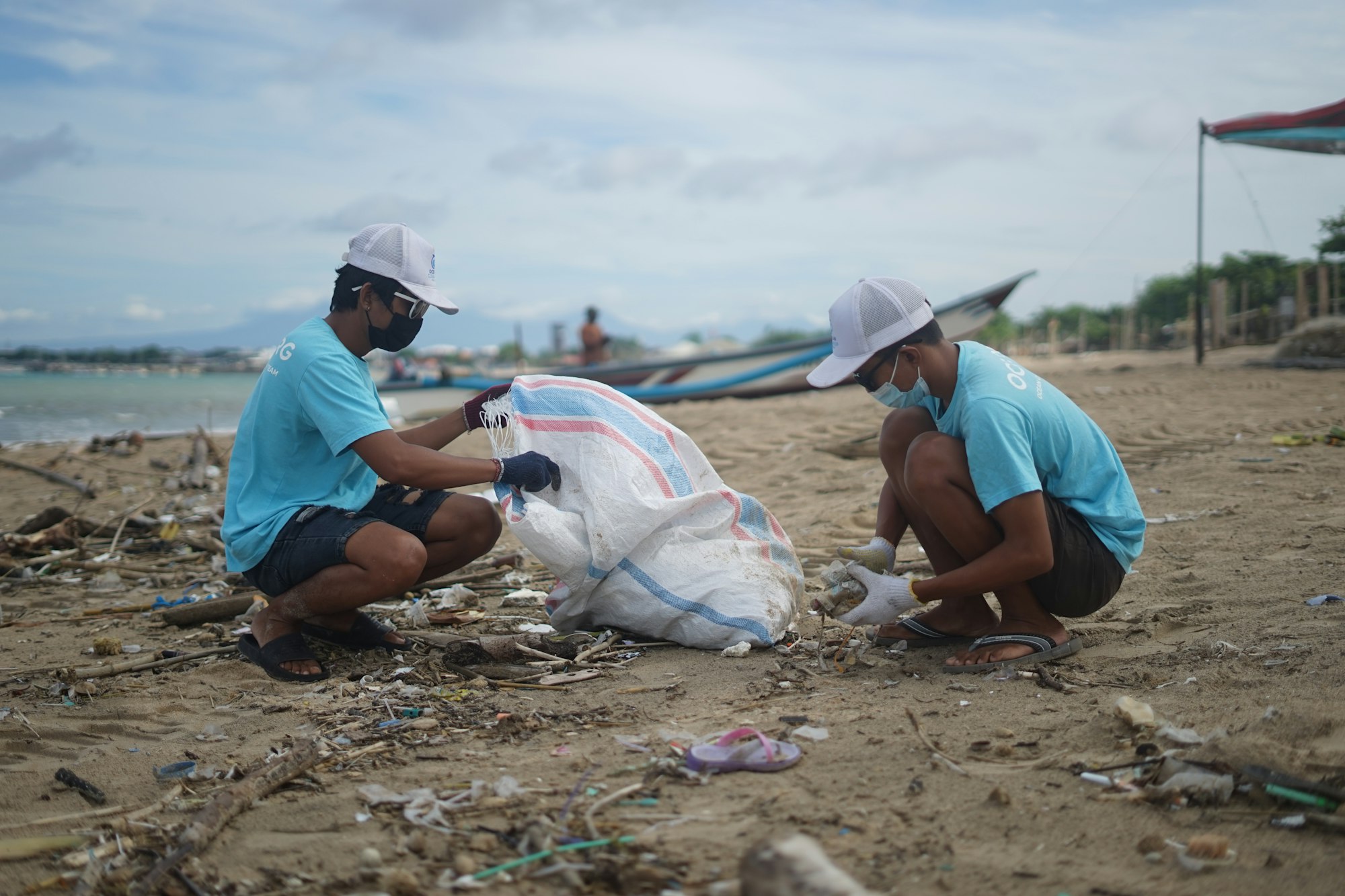 Two Indonesian males clean the beach on behalf of ocean cleanup group. OCG is a free ocean search engine that cleans the ocean. 