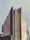 A tall, modern skyscraper with a unique, terraced glass facade reflecting the light. The building has multiple tiers that appear to taper as they ascend. The lower part of the image shows the rooftop of another building with a green trim. The sky is overcast, giving the scene a muted color palette.