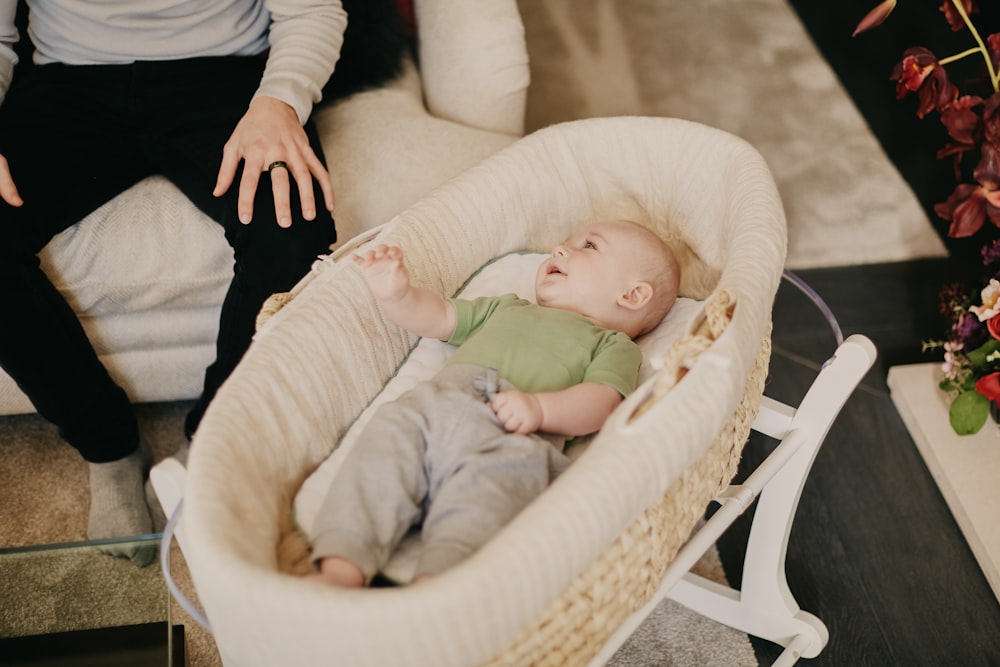 白と茶色のベビーベッドに横たわっている緑のワンジーの赤ちゃん