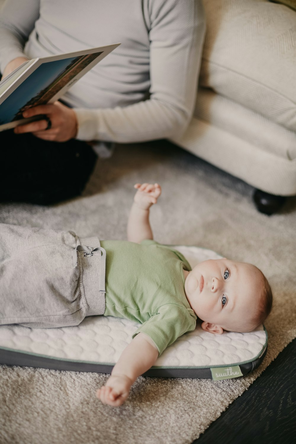 baby in green onesie lying on floor