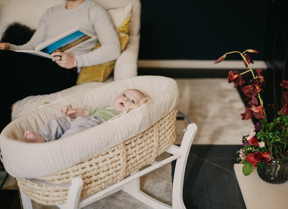 Bébé en onesie blanc et rose allongé sur un berceau en osier blanc