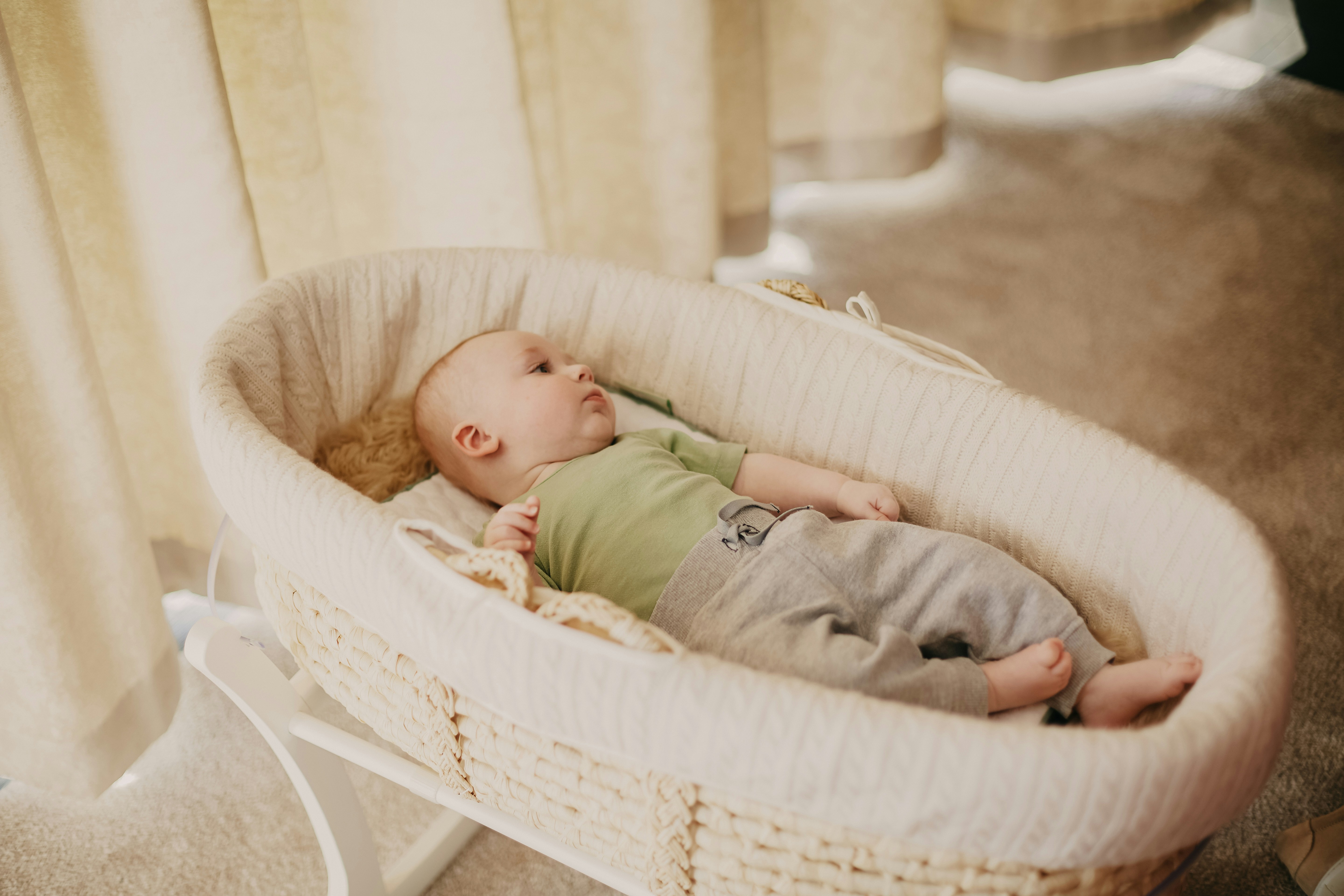 baby in green onesie lying on white wicker crib