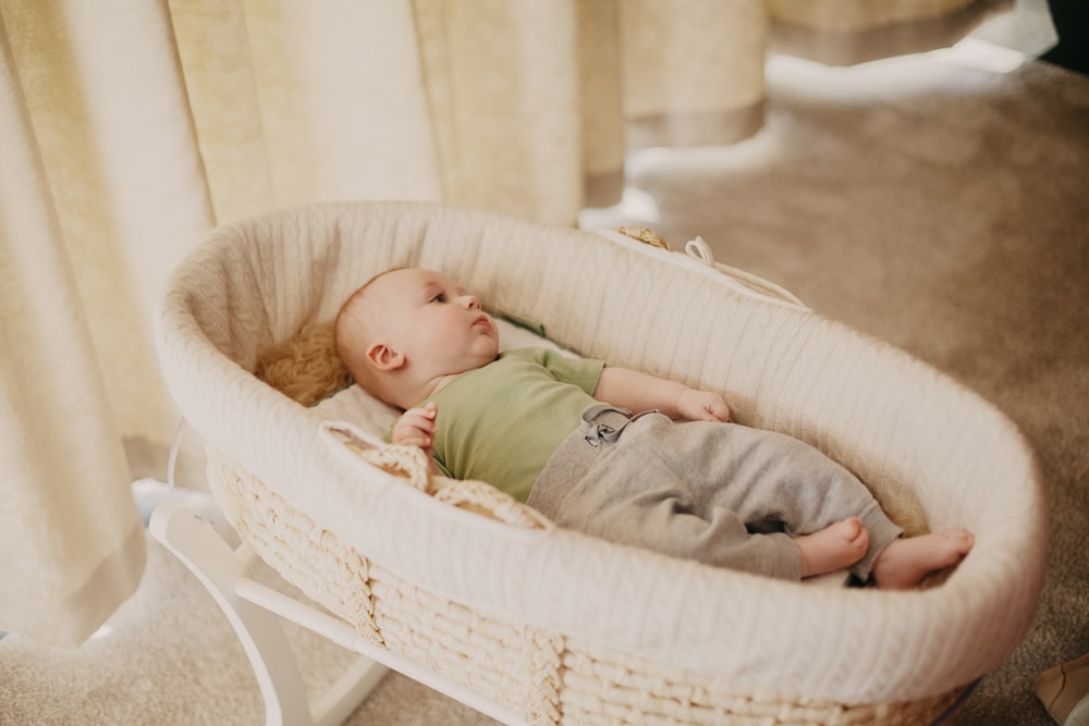 baby in green onesie lying on white wicker crib