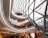 An abstract architectural interior featuring a modern, spiraling design with several levels. The ceiling is composed of a geometric pattern of glass and metal, letting in ample light and creating reflections. The structure blends curves and lines in a dynamic fashion, and the interior spaces feature warm lighting and open areas.
