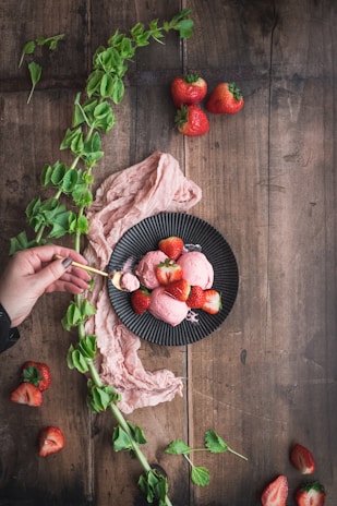 An overhead shot of a rustic wooden table scattered with fresh fruits and a bowl of babe ice cream melting slowly.