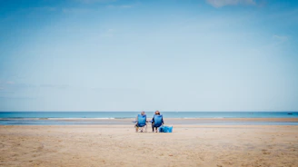 2 person sitting on beach sand during daytime