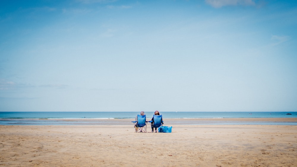 2 personas sentadas en la arena de la playa durante el día