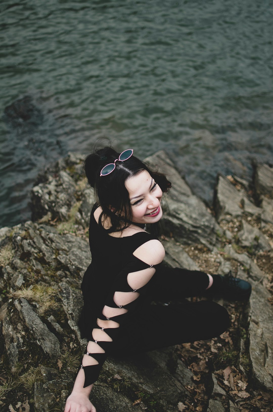 woman in black tank top and black pants sitting on rock near body of water during