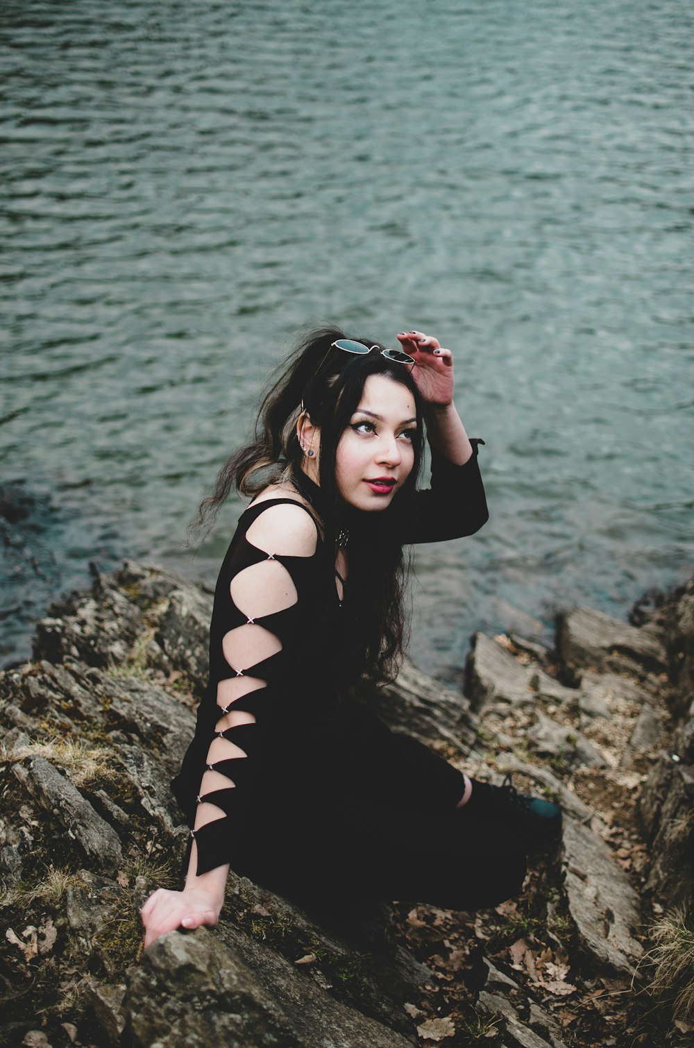 woman in black long sleeve shirt sitting on rock near body of water during daytime