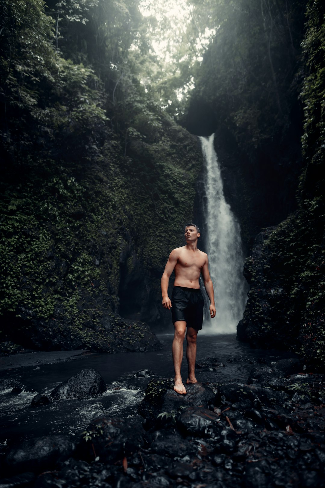 man in black shorts standing on rocky river during daytime