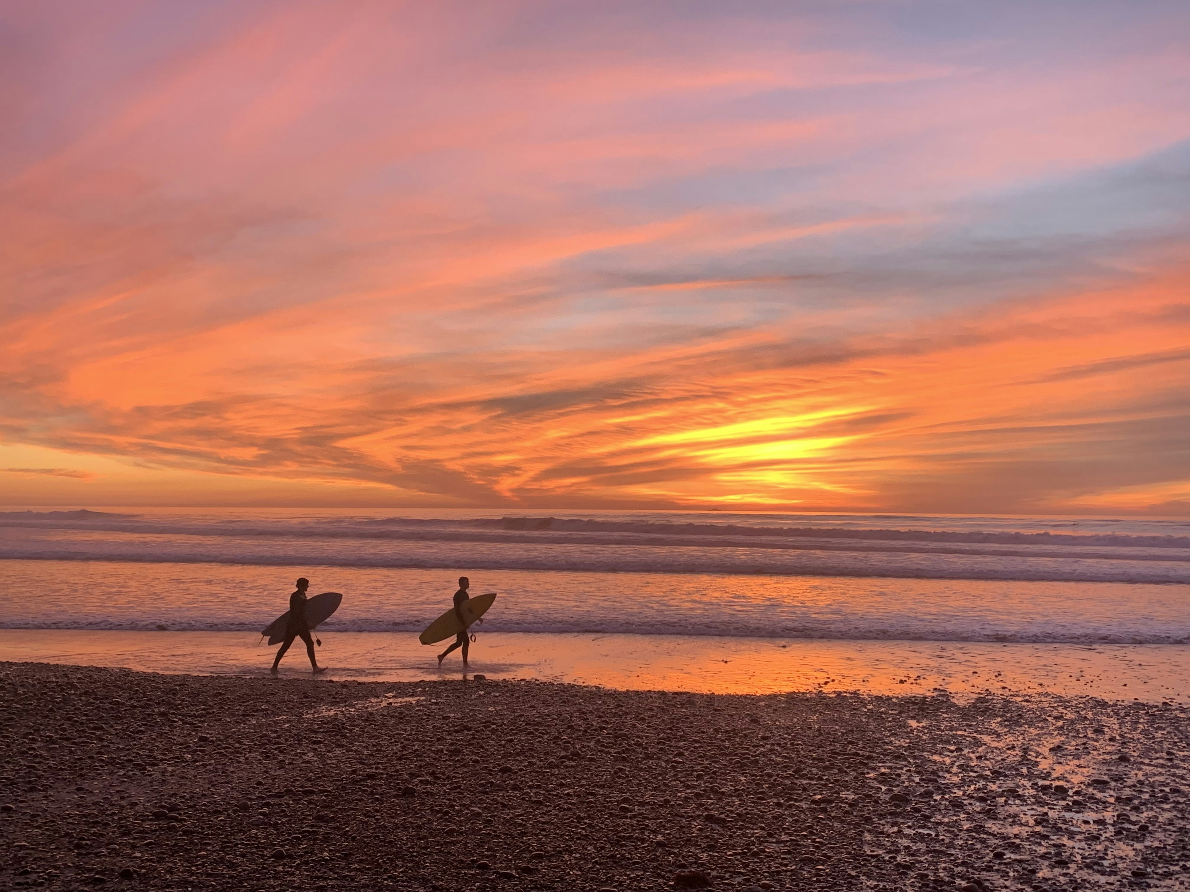 2 people walking on beach during sunset