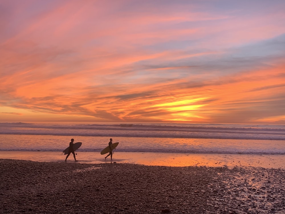 2 people walking on beach during sunset