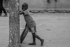 grayscale photo of boy in t-shirt and shorts standing on tree trunk