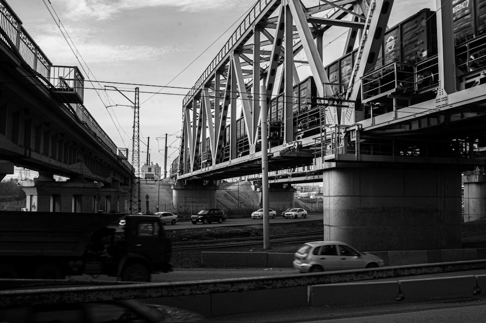 grayscale photo of cars on road under bridge