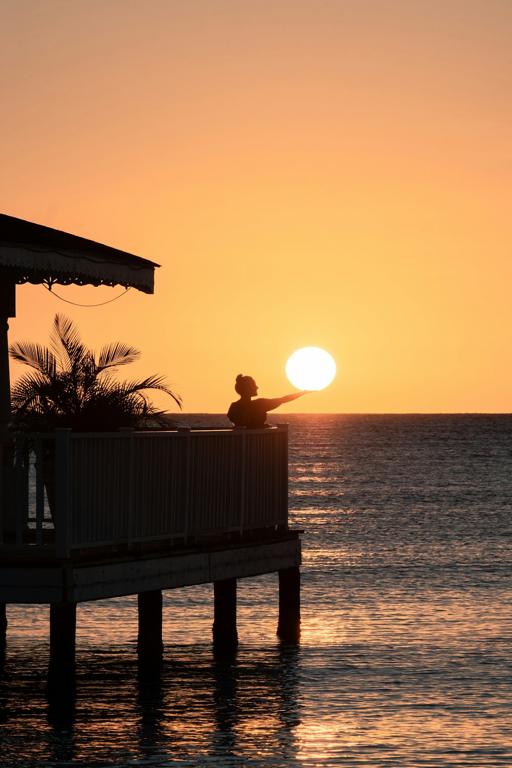 the sun is setting over the ocean with a pier in the foreground