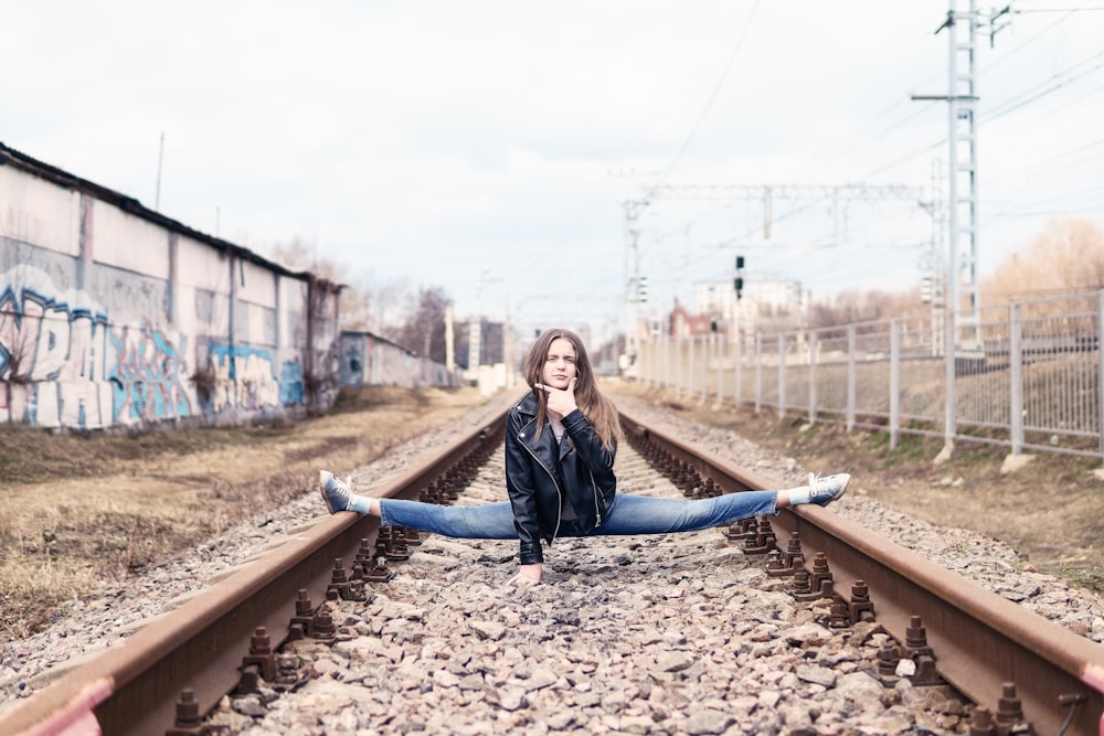 woman in black leather jacket sitting on train rail during daytime